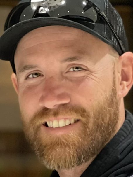 Smiling man with a beard and sunglasses, wearing a black cap.
