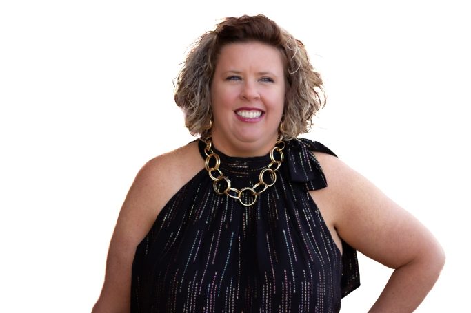 Smiling woman with curly hair wearing a black top and a chunky gold necklace.