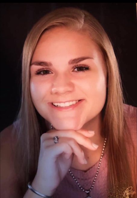 Young woman smiling, with long blonde hair and resting her chin on her hand.